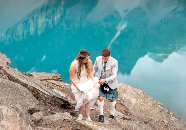 Scottish groom taking care of his wife's wedding dress while going up the hill after their elopement at Moraine Lake