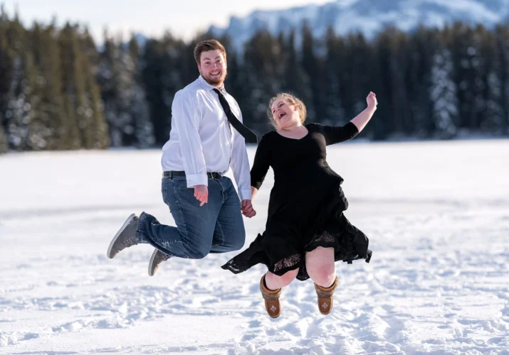 Happy couple in love jumps at the frozen Two Jack Lake in Banff.