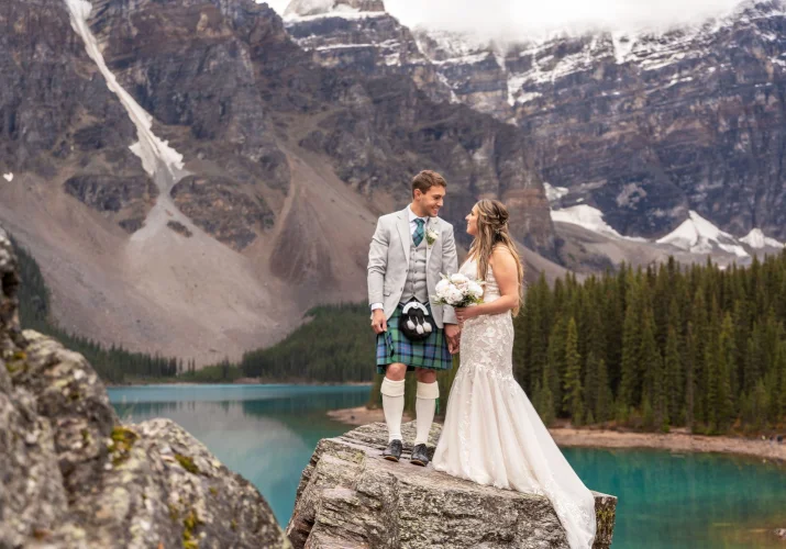 Newlyweds look at each other surrounded by Rocky Mountains at Moraine Lake in Banff.