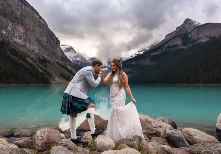 Groom kissing the bride's hand during elopement ceremony at Lake Louise.