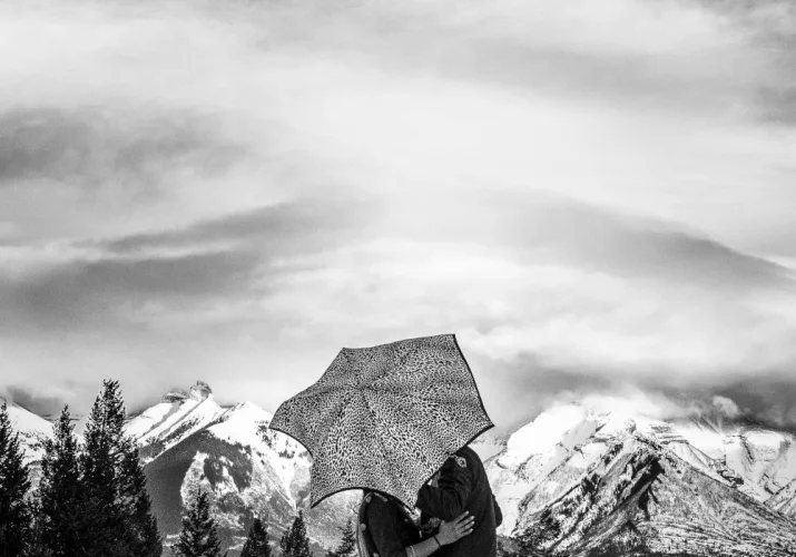 Grom and bride are kissing under an umbrella.