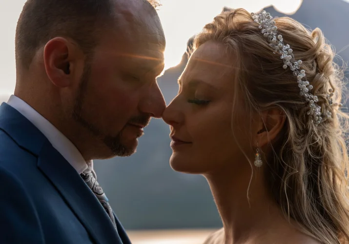 Newly married couple touching theis noses. Rays of the sun between their heads. Romantic after wedding photo shoot in Banff.