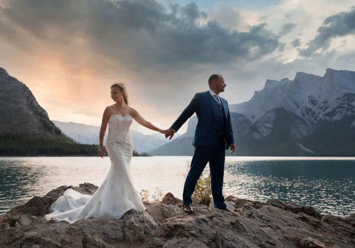 After wedding session at Lake Minnewanka during stunning sunrise. Marrieg couple holding hands.