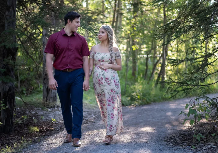 Future parents walking in forest in Banff. They look at each other. Pregnant woman touches her belly.