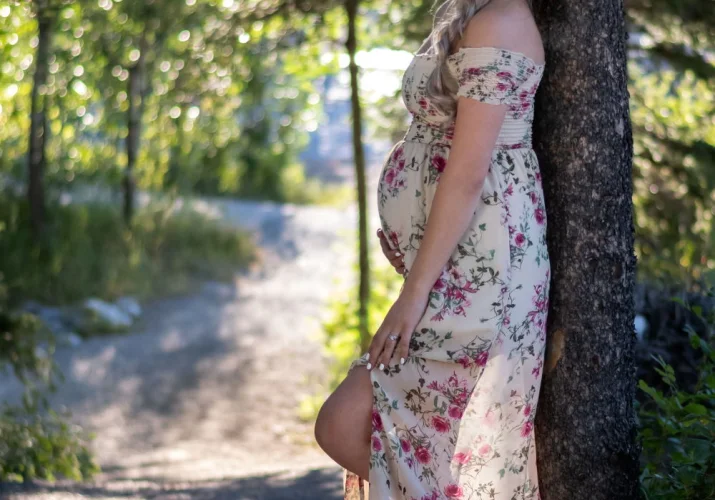 Pregnant woman posing during materning photo shoot in Banff. She lean against the tree and touch her belly.