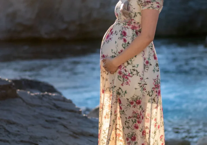 Maternity portrait in Banff. Pregnant woman touches her bally and smiles at the camera.