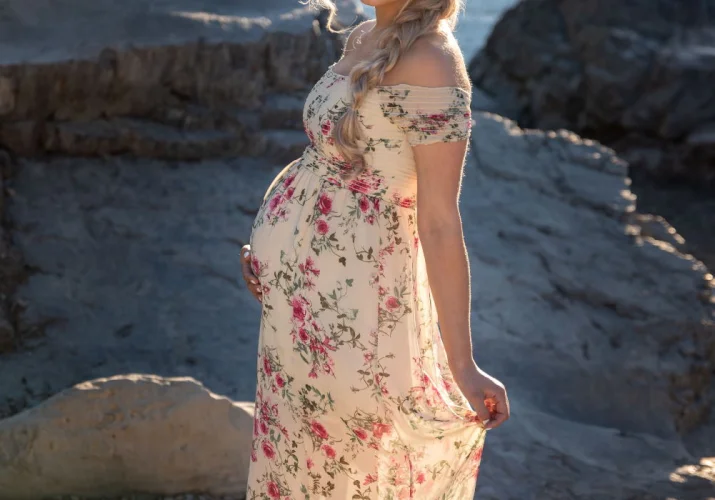 Proud pregnant woman touches her belly and smiles at the camera during maternity photo session in Banff.