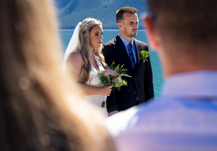 Elopement ceremony at Minnewanka Lake . Bride and groom listening Pastor's speech.