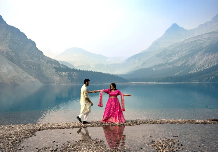 Indian engaged couple is dancing at Bow Lake. They are wearing traditional outfit in pink and gold colors.