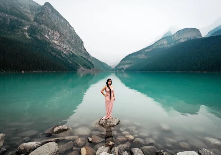 Woman in a pink long dress is standing on the rock at the Lake Louise. She is posing for Banff Wedding Photographers.