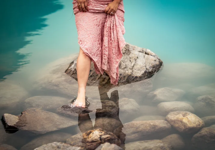 Woman in pink dress is jumping from the rock at Lake Louise. She is barefoot.