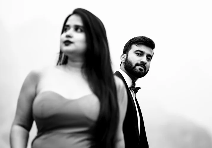 Man is looking at the camera and his fiancee is looking away. Black and white photography.