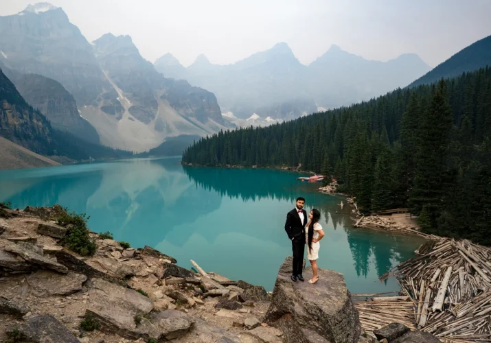 Dressed couple standing at the huge rock at Moraine Lake. They are happily dancing. e