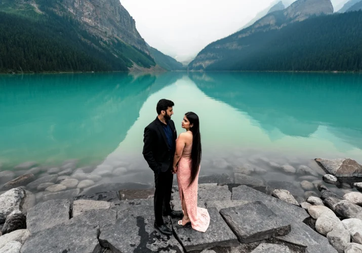 engagemant portrait an Lake Louise . The couple look at each other. Lady wears a pink dress and gentleman wears a black suite