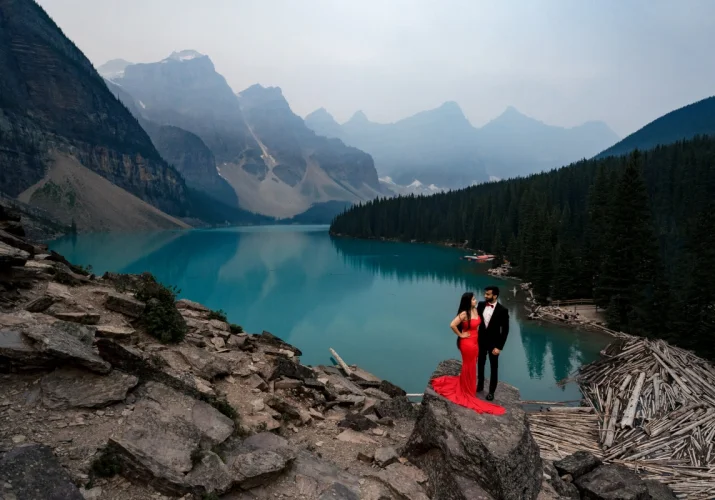Engagement session at Moraine Lake in Banff. The couple standing on a giant rock. They are surrounded by the Canadian Rockies and turquoise lake