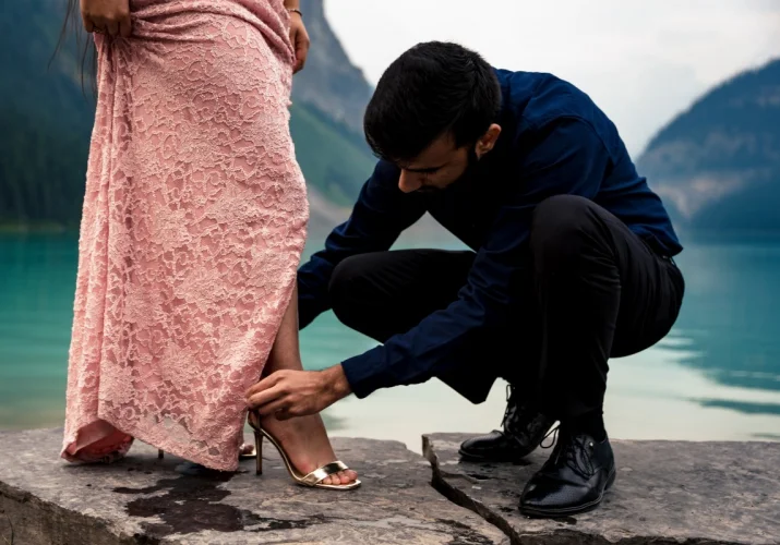 Indian man helping his fiancé to fixing her shoes before their engagement session at Lake Louise