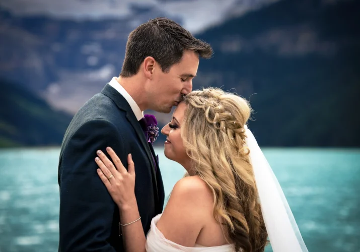 Groom is kissing the bride at the forehead.
