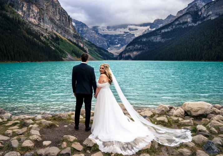 Newlyweds portrait taken at Banff Wedding. Bride looks at the camera, groom admire stunning view at Lake Louise.