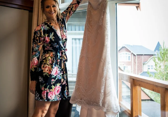 bride is reaching her wedding dress hanging at the window