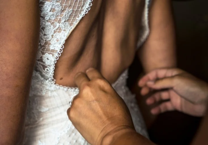 Bridesmaid zipping bride's wedding dress.