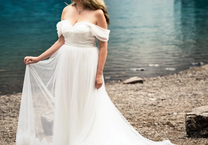 Bride's portrait taken by the Lake. She looks ahead holding her dress.