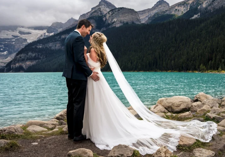 Bride and groom portrait by the Lake Louise. Couple look deeply on each other.