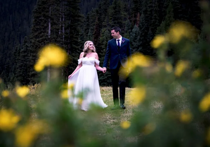 Bride and groom walk in the garden in Fairmont Hotel in Lake Louise. They look at each other surrounded by the yellow flowers.
