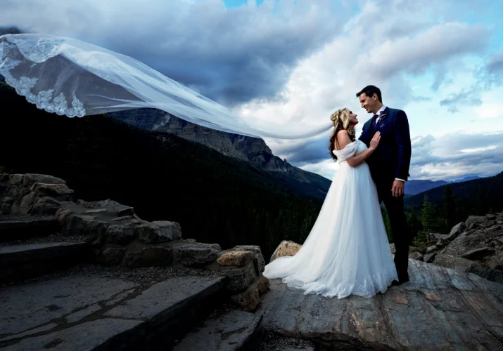 Adventures newlyweds standing at the rock and looking at each other. Bride's veil is blown by air.