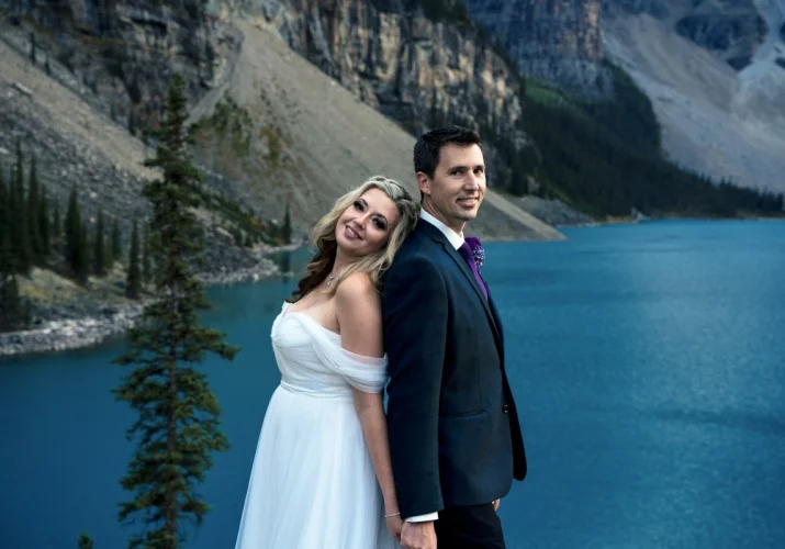 Newlyweds standing back to back and smile at the Banff Wedding Photographer camera.