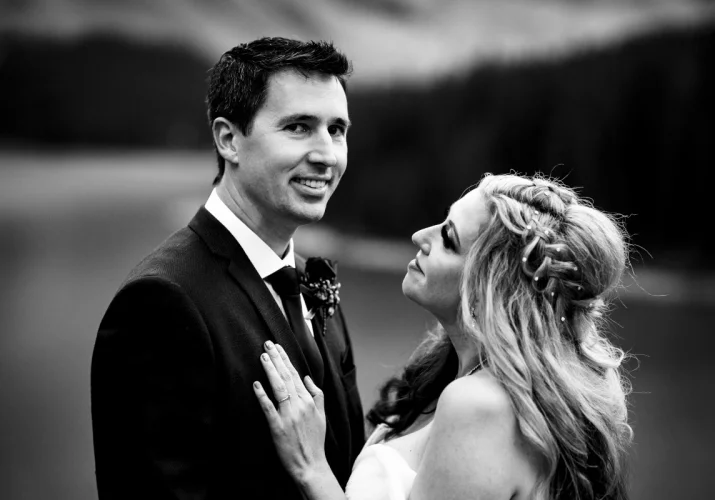Newlyweds portrait in black and white. Bride looks at the groom with love. Groom looks at the Banff Wedding Photographer camera.
