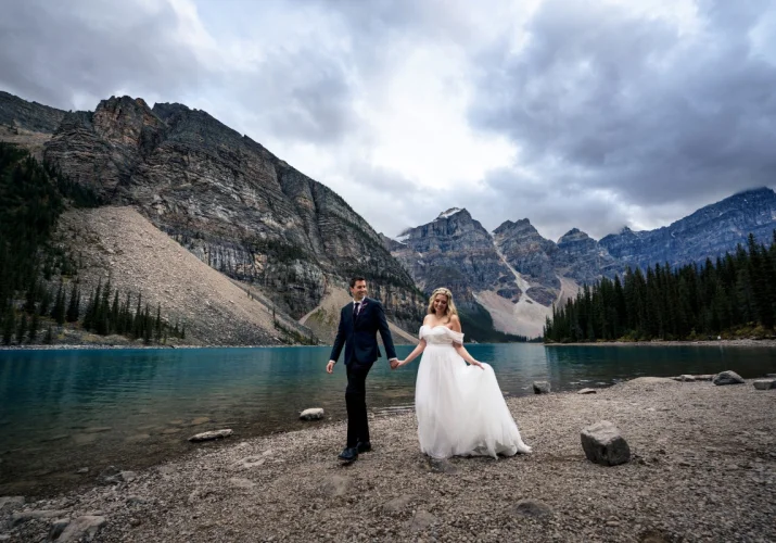 Wedding photo session at Moraine Lake captured by Banff Wedding photographer. Newlyweds walk down the lake and holds their hands.