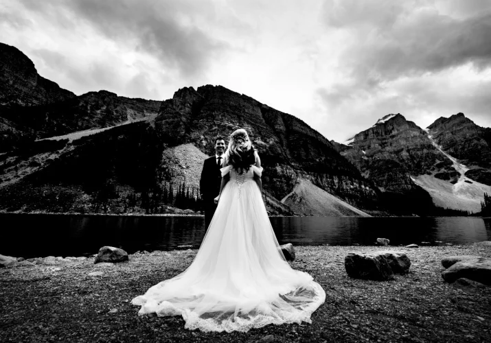 Black and white photograph of newlyweds. Bride wears long stunning dress. Groom admire her beauty.