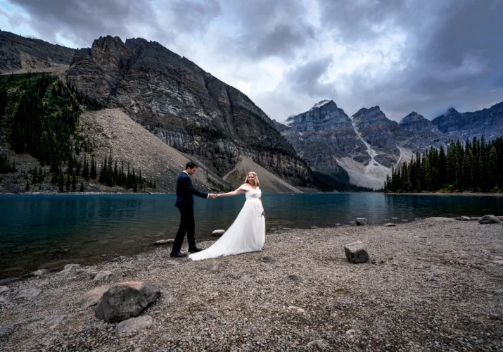 Newlyweds walk down the Moraine Lake. They holds their hands.