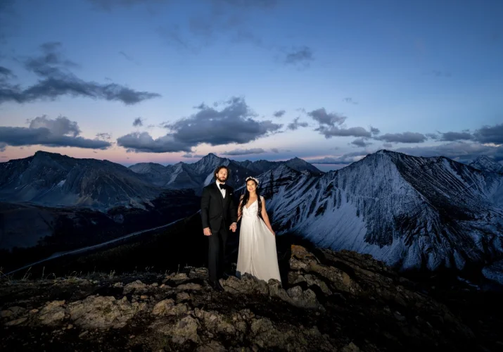 Fearless wife and husband posing at the top of the mountain in Banff .