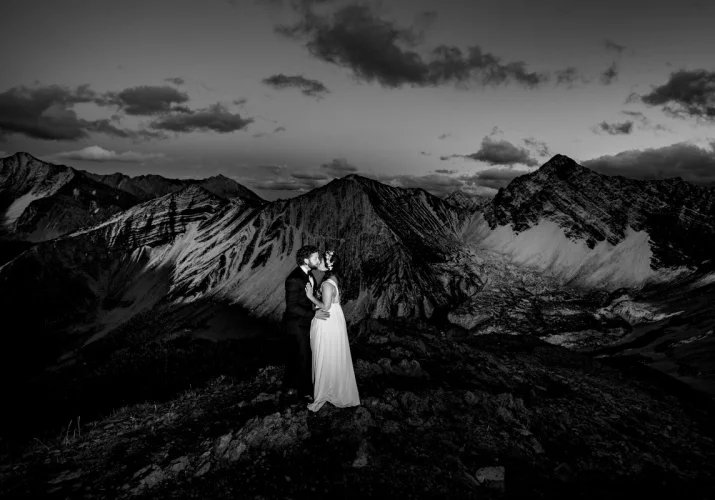 Newlyweds kissing on the peak of the Canadian Rockies while Banff Wedding Photographer capture unique moments.