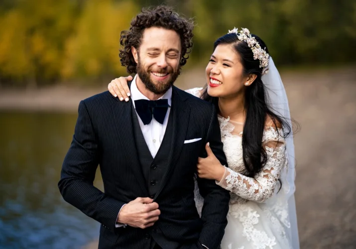 Bride is whispering something to her husband. Groom is laughing.