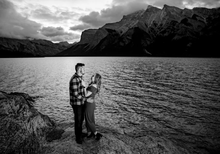 Banff Wedding Photographer caotured newly engaged couple looking at each other with love. They are at the lake surrounded by the Canadian Rockies.