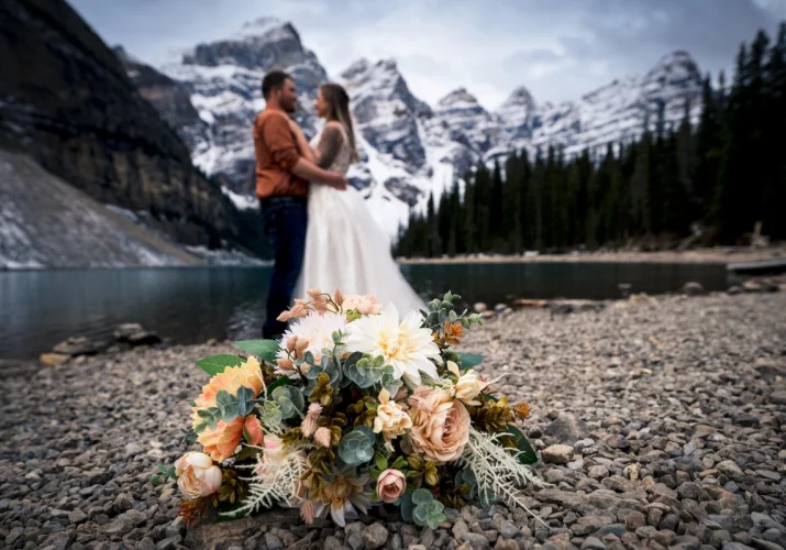 Mountain photo session taken by Calgary Wedding Photographer. Groom and Bride look at each other while bouquet is on the ground. They are at Moraine Lake in Banff National Park.