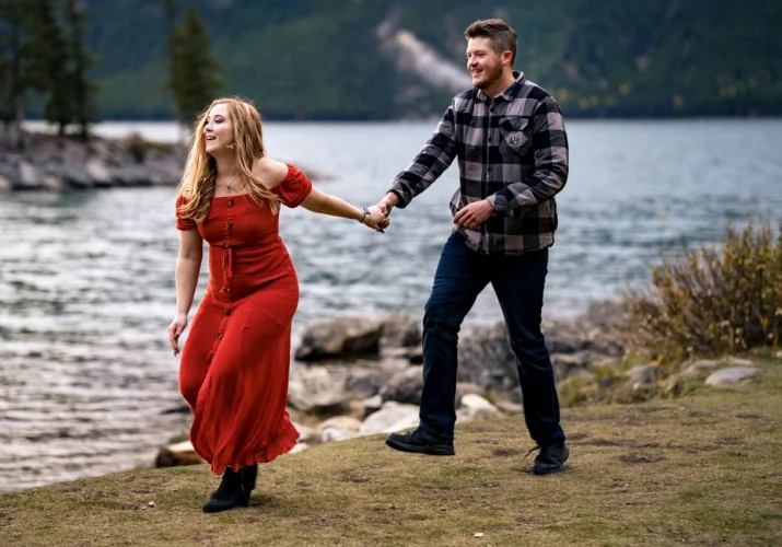 couple in love run and have fun at Minnewanka Lake in Banff. They hold their hands and laugh.