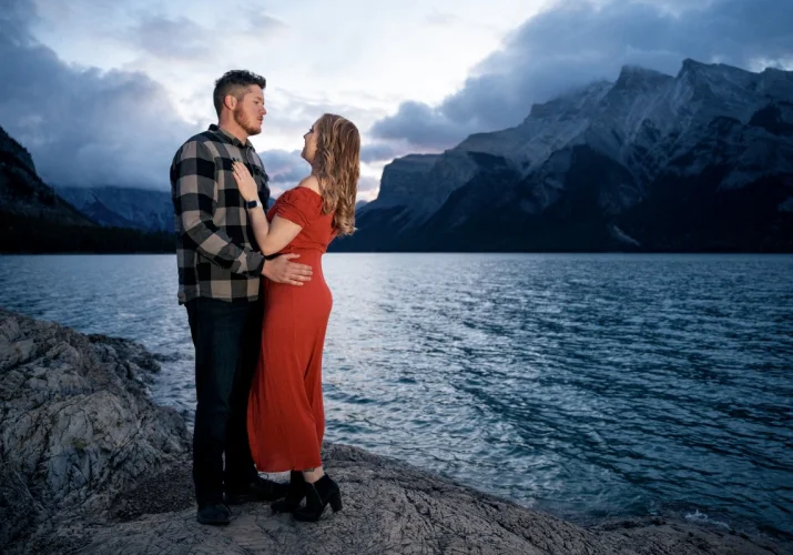 Engagement photo session taken by Calgary Wedding Photographer. Couple in love are hugging at look at each other. They are at the Minnewanka Lake in Banff.