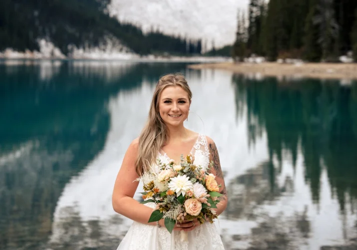 Bride's portrait at Moraine Lake in Banff. Bride holds colourful flowers.