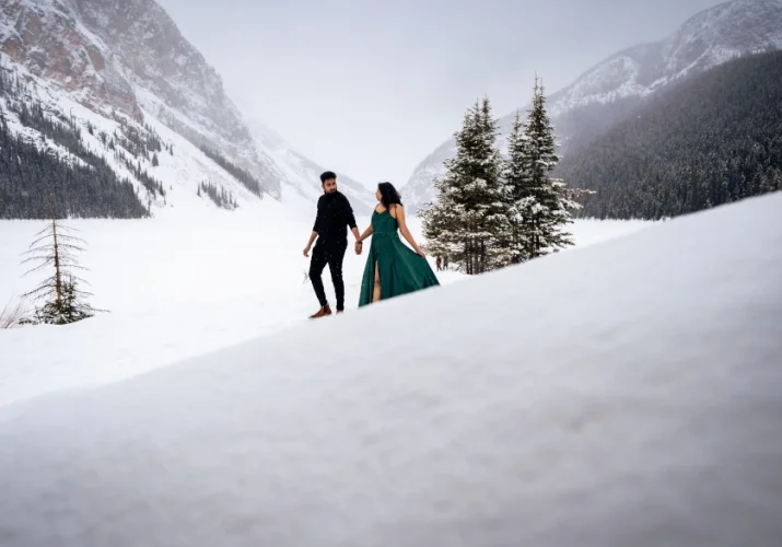 Couple in love walks down the hill at Lake Louise in wintertime. She wears green, long dress, he is dressed n black.