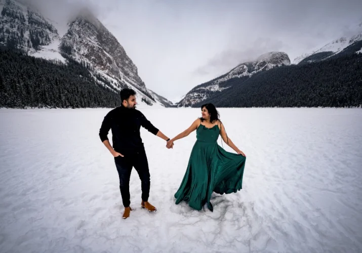 Indian couple walk on frozen Lake Louise during their photo session with the best Calgary Wedding Photographer. They hold hands and look at each other.