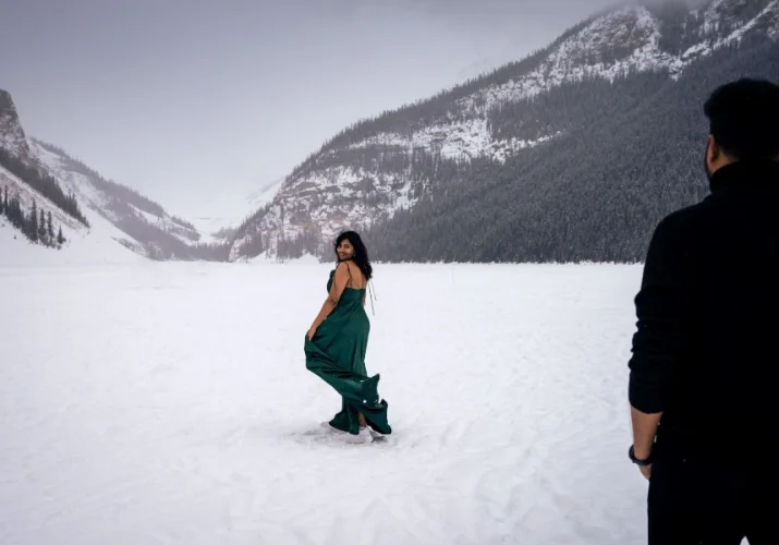 Lady dance and look charming at her husband. She dances on the frozen lake which is covered with snow. Behind her ate the Canadian Rocky Mountains.