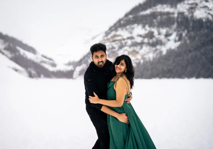Indian couple smiling and looking at the calera of Calgary Wedding Photographer. Winter photo session at Lake Louise in Banff.
