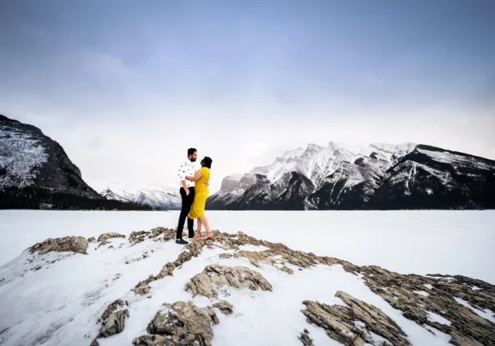 Couple in love stand on island at Minnewanka Lake. during winter. They hug each other.