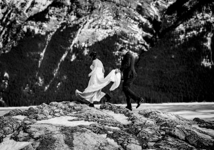 Groom holds bride's wedding dress while they climb in the Canadian Rockies.