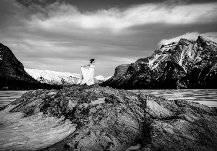 Bride's portrait in black and white. She stands at the giant rock at frozen Minnewanka Lake in Banff.
