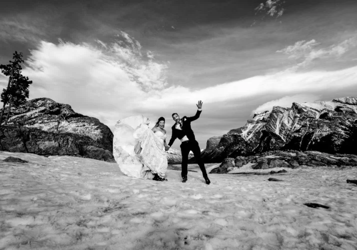 Groom and bride have hun during their photo session at Minnewanka Lake. They jump high and lough.