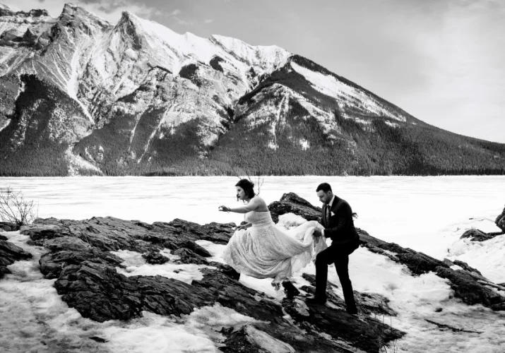 Bride and groom climb the mountain during winter. Dride wears hikking boost and wedding dress.